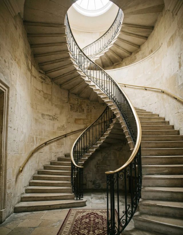 A spiral stone staircase with a brass handrail, seen from below, with daylight from a skylight