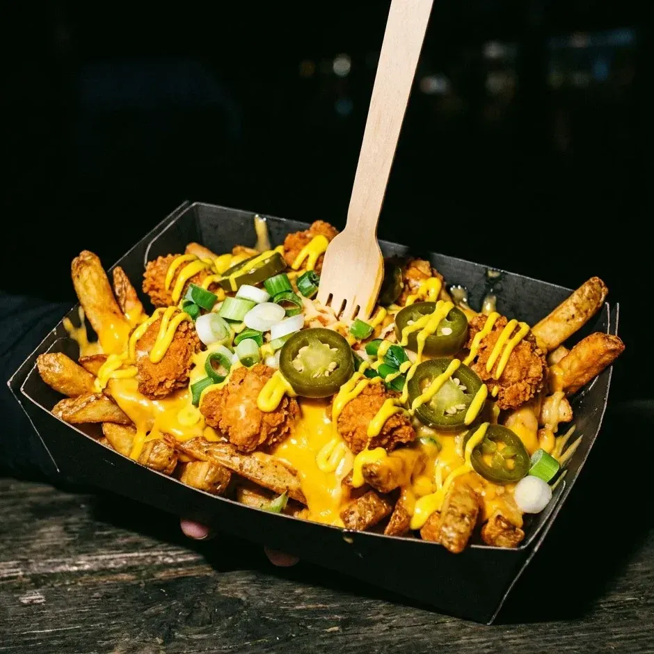 Loaded fries with cheddar sauce, crispy chicken, jalapeños and spring onion, a wooden fork stuck in.