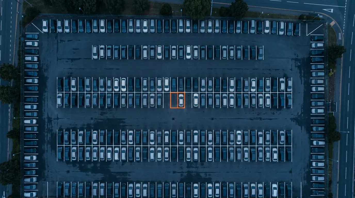 Aerial view of a rental car lot at dusk with white-lined bays, one bay outlined in orange